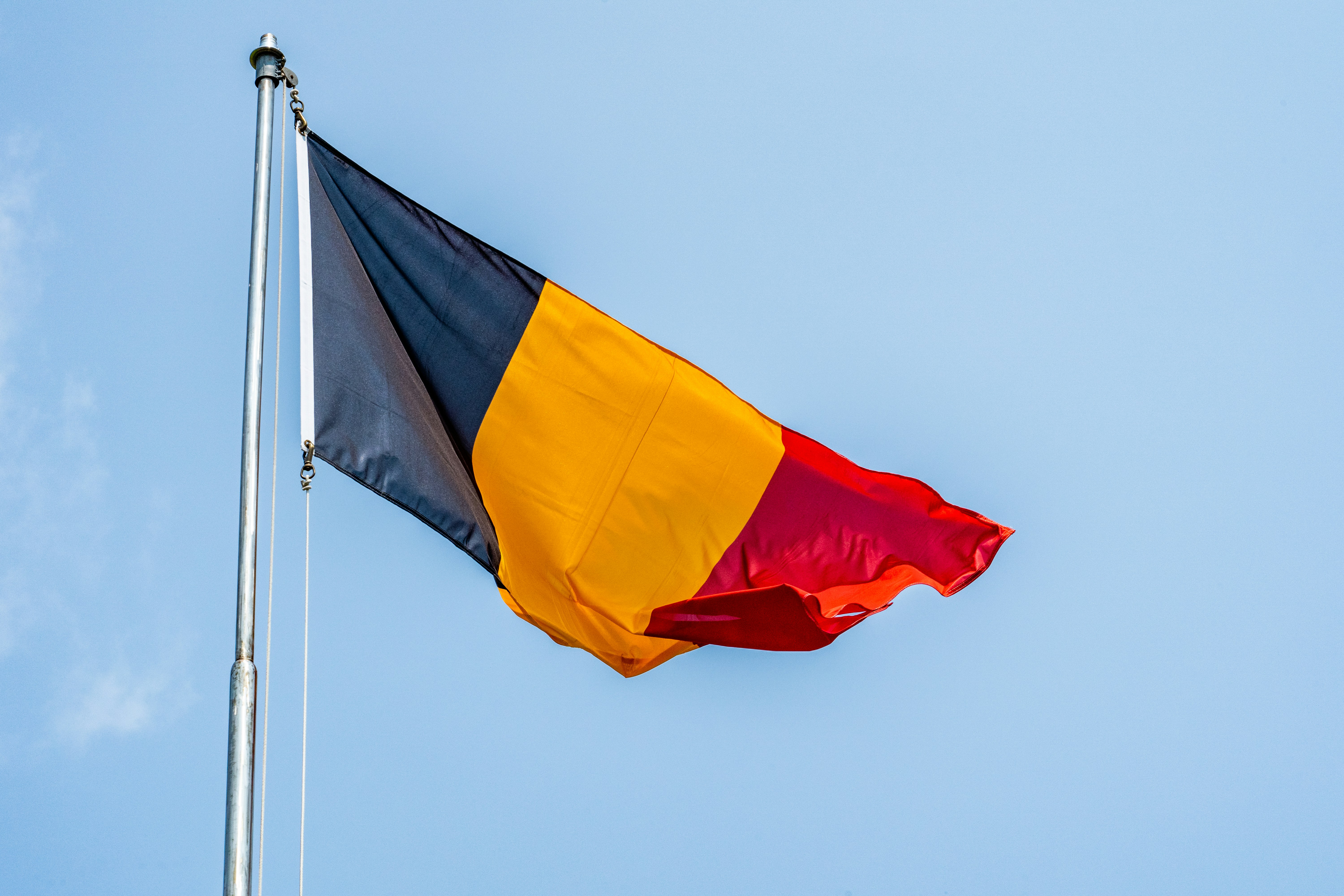 Belgische Flagge in Schwarz, Gelb und Rot weht vor blauem Himmel